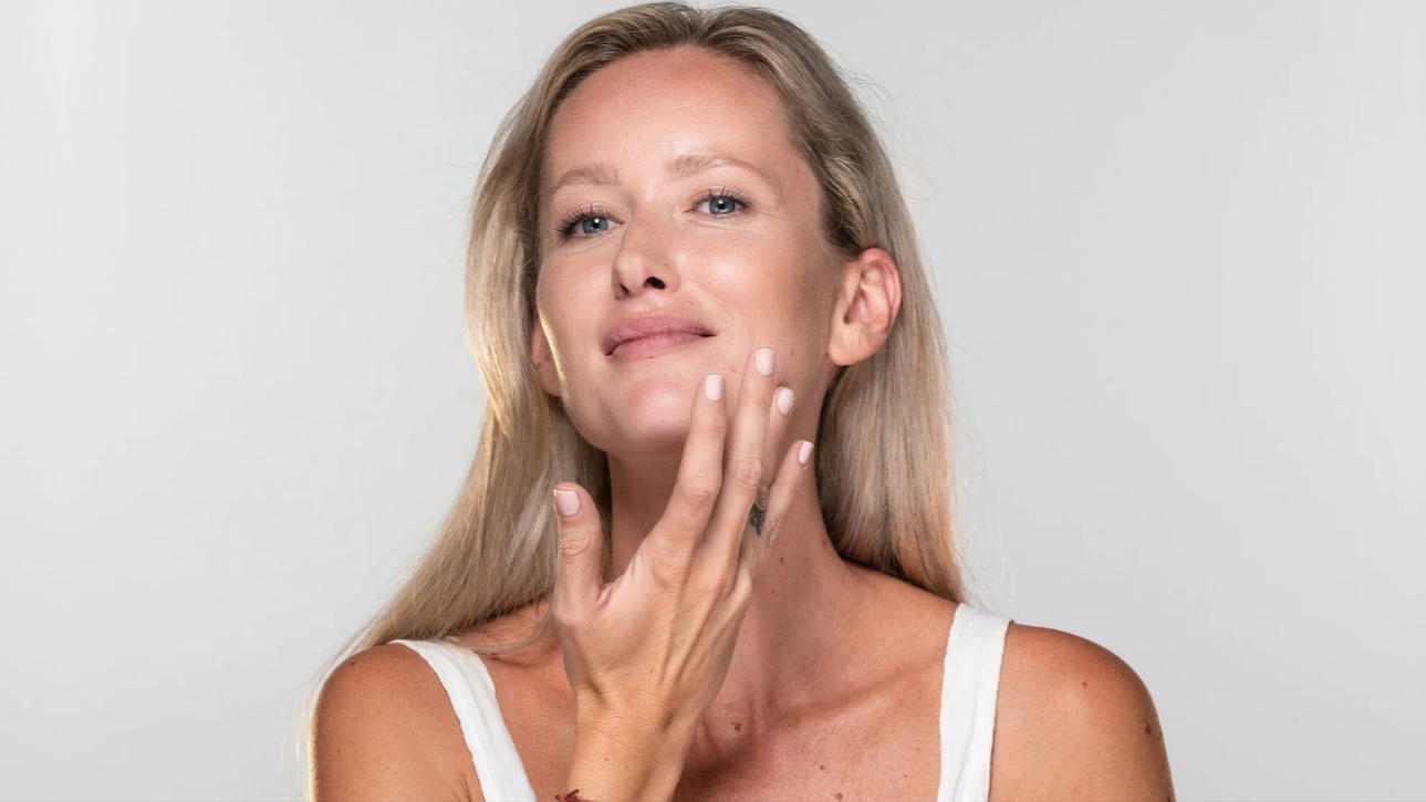 Woman touching her face against a plain background using face mask