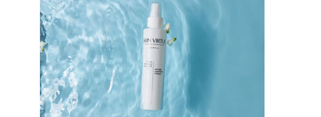 A white spray bottle labelled SKIN VIRTUE Future Advanced Serumist® stands upright against a bright blue water-texture background with bubbles and a small white flower accent.