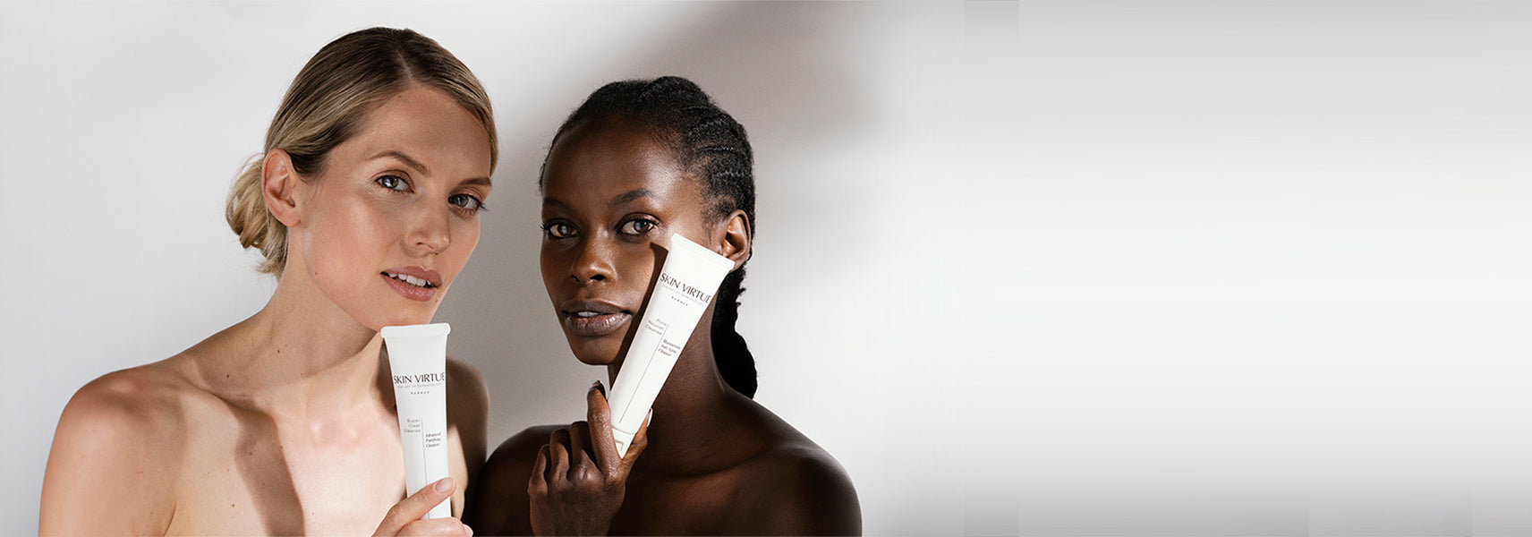 Black and white women holding Skin Virtue skincare products to there faces against a white background